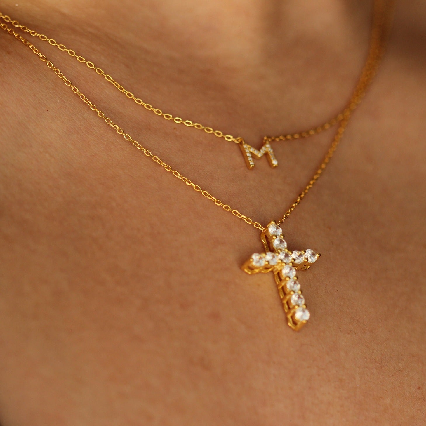 gold letter necklace stacked with gold cross necklace on models neck