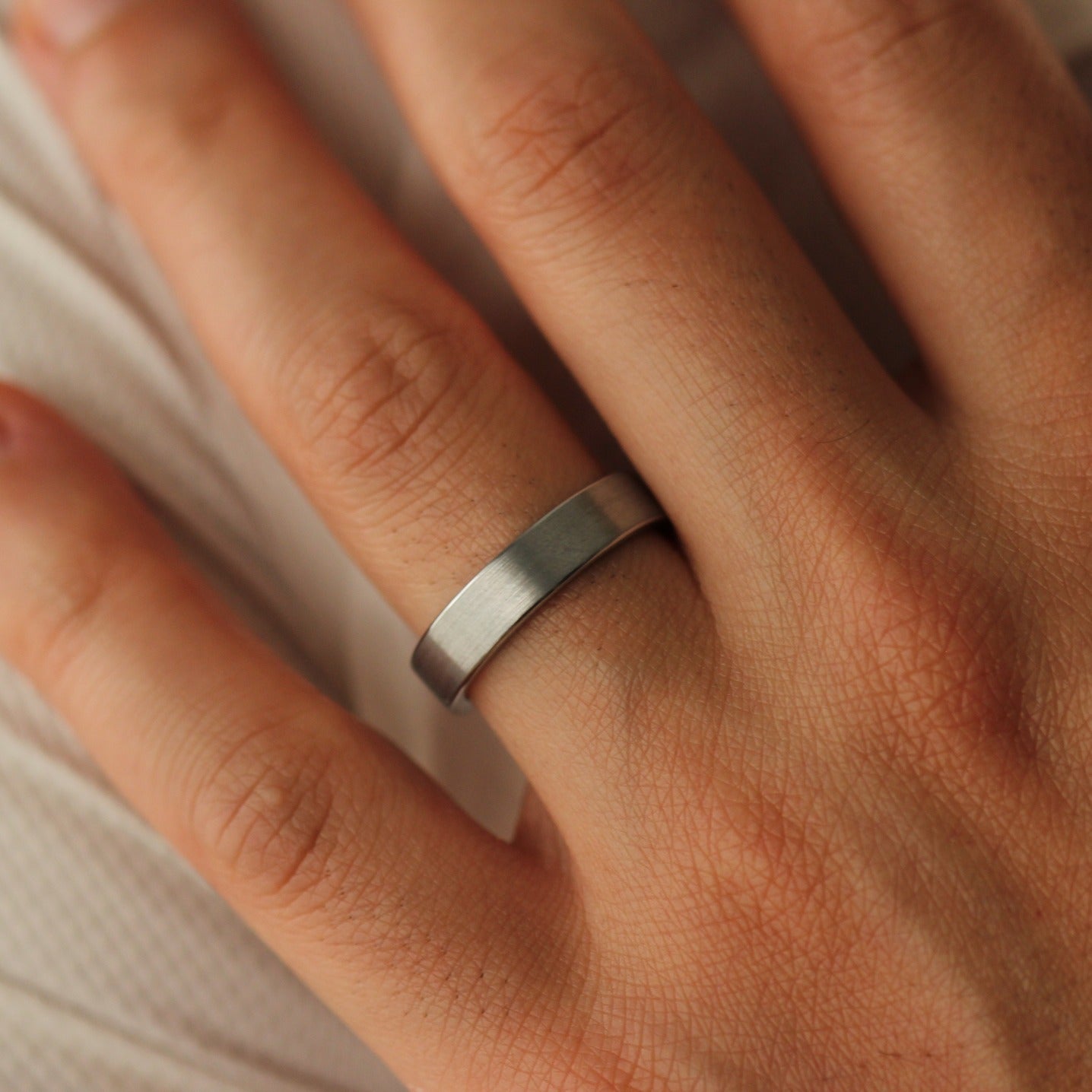 Close-up of a man's hand wearing a brushed silver ring on a neutral background