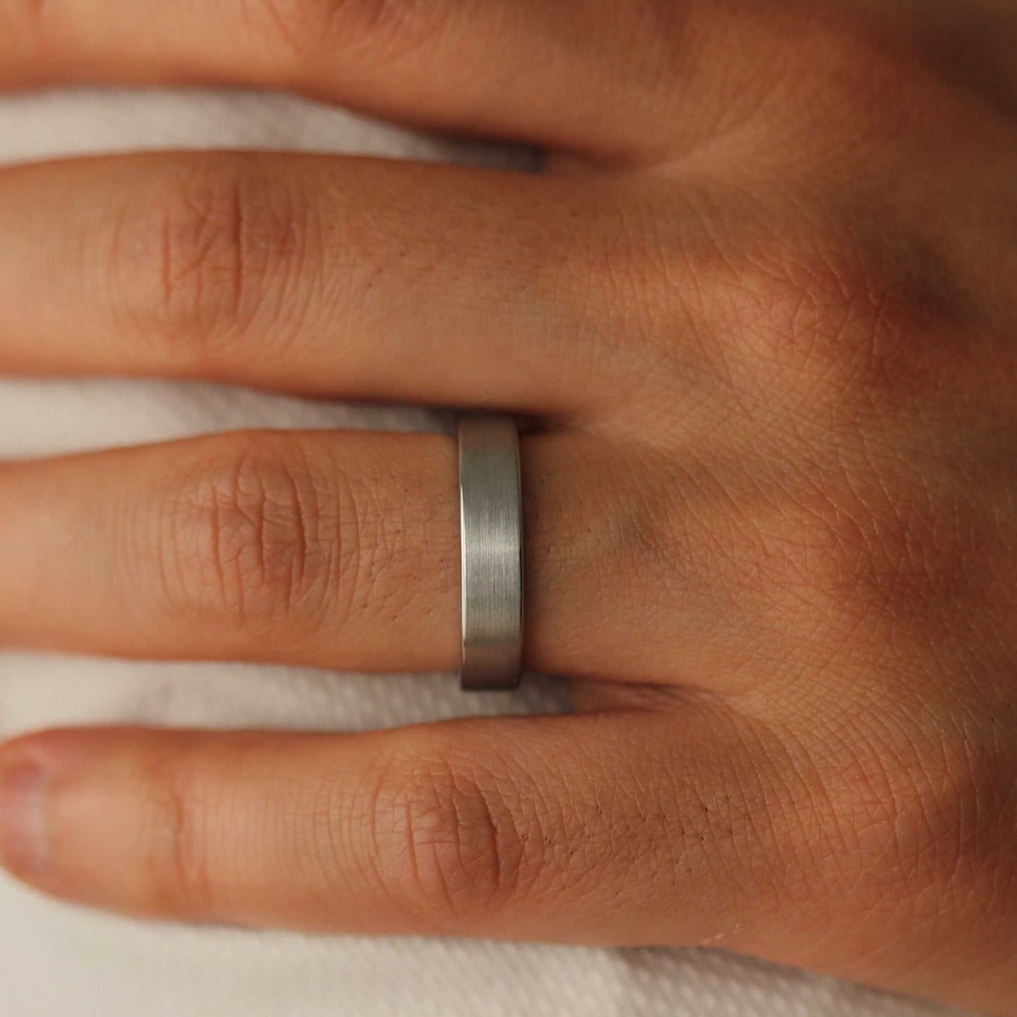 Brushed Silver wedding flat band on a person's finger with a neutral background