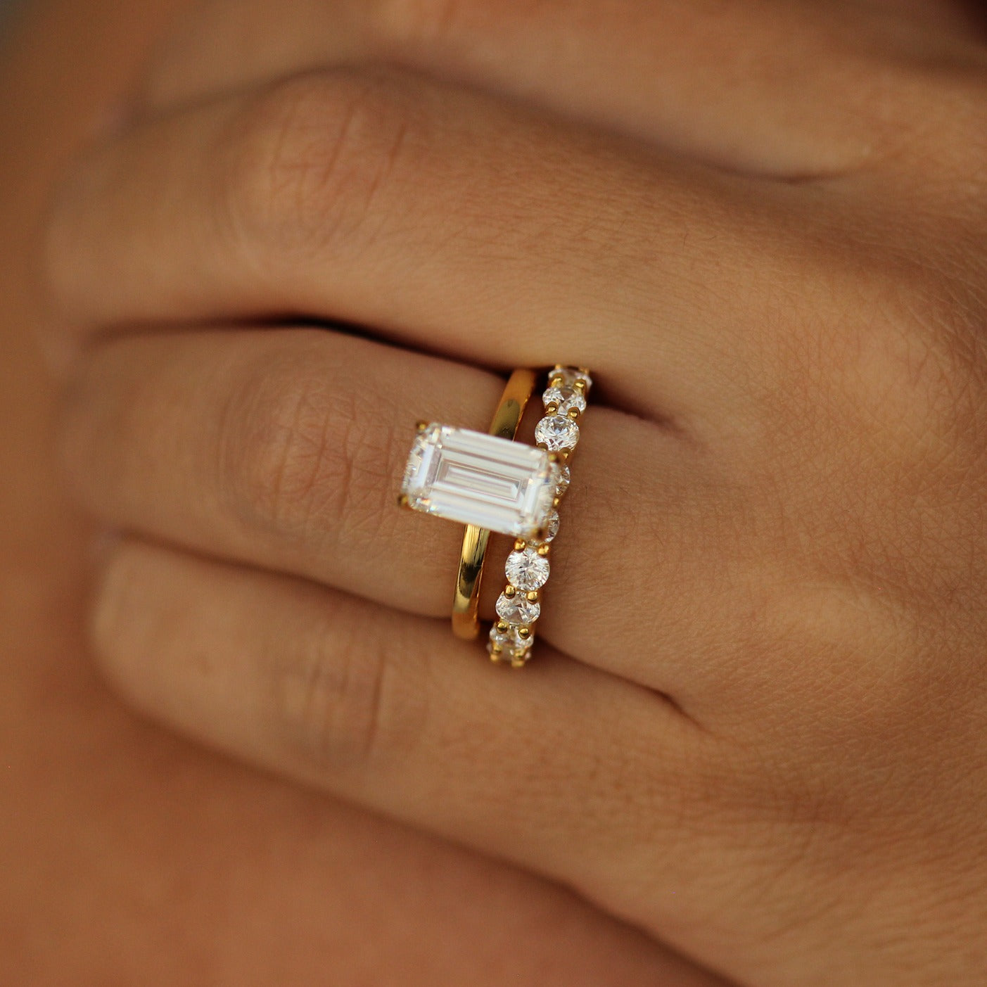 plain gold ring with emerald centre stone on hand and 18k gold stacking ring