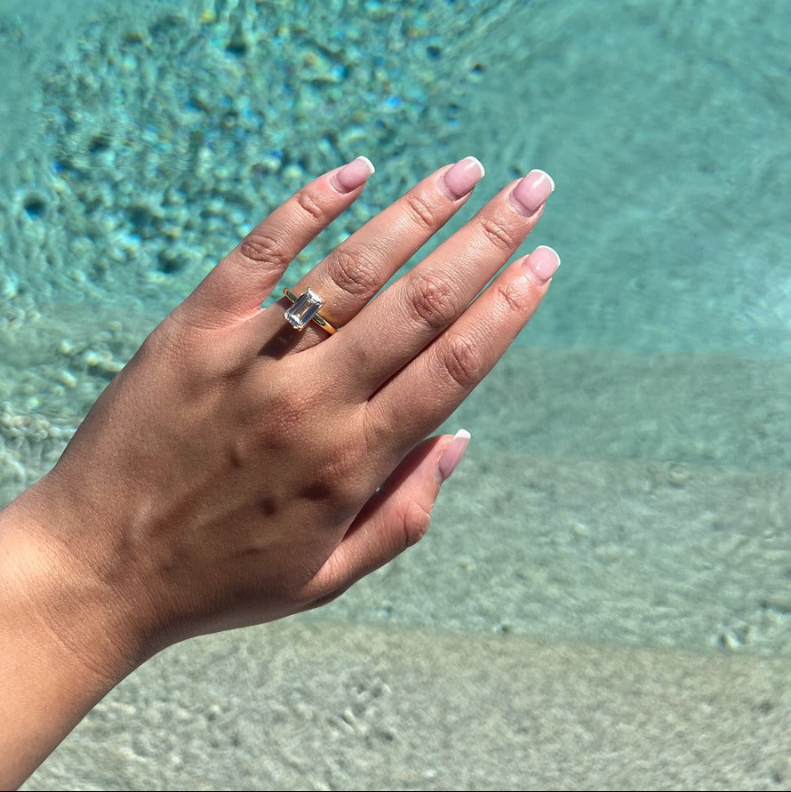plain gold ring with emerald centre stone with pool in background