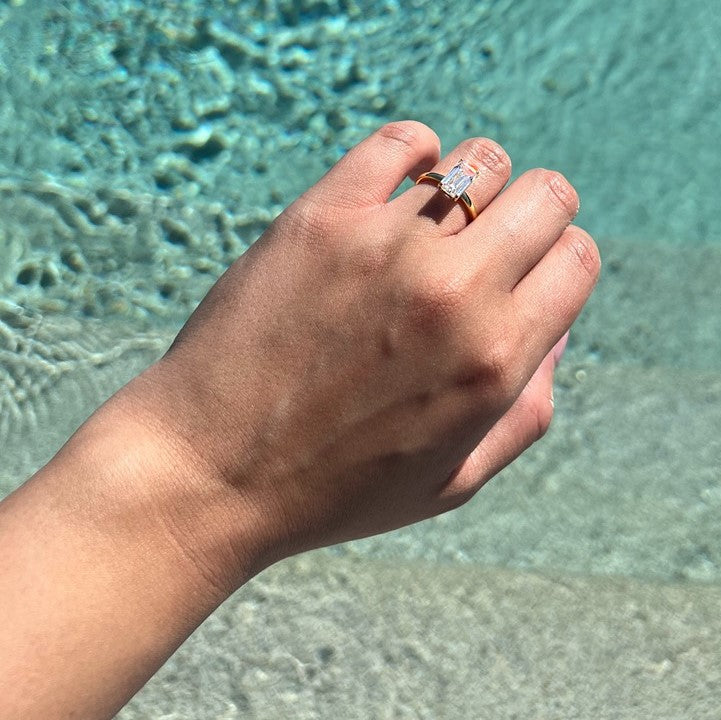 plain gold ring with emerald centre stone with pool in background