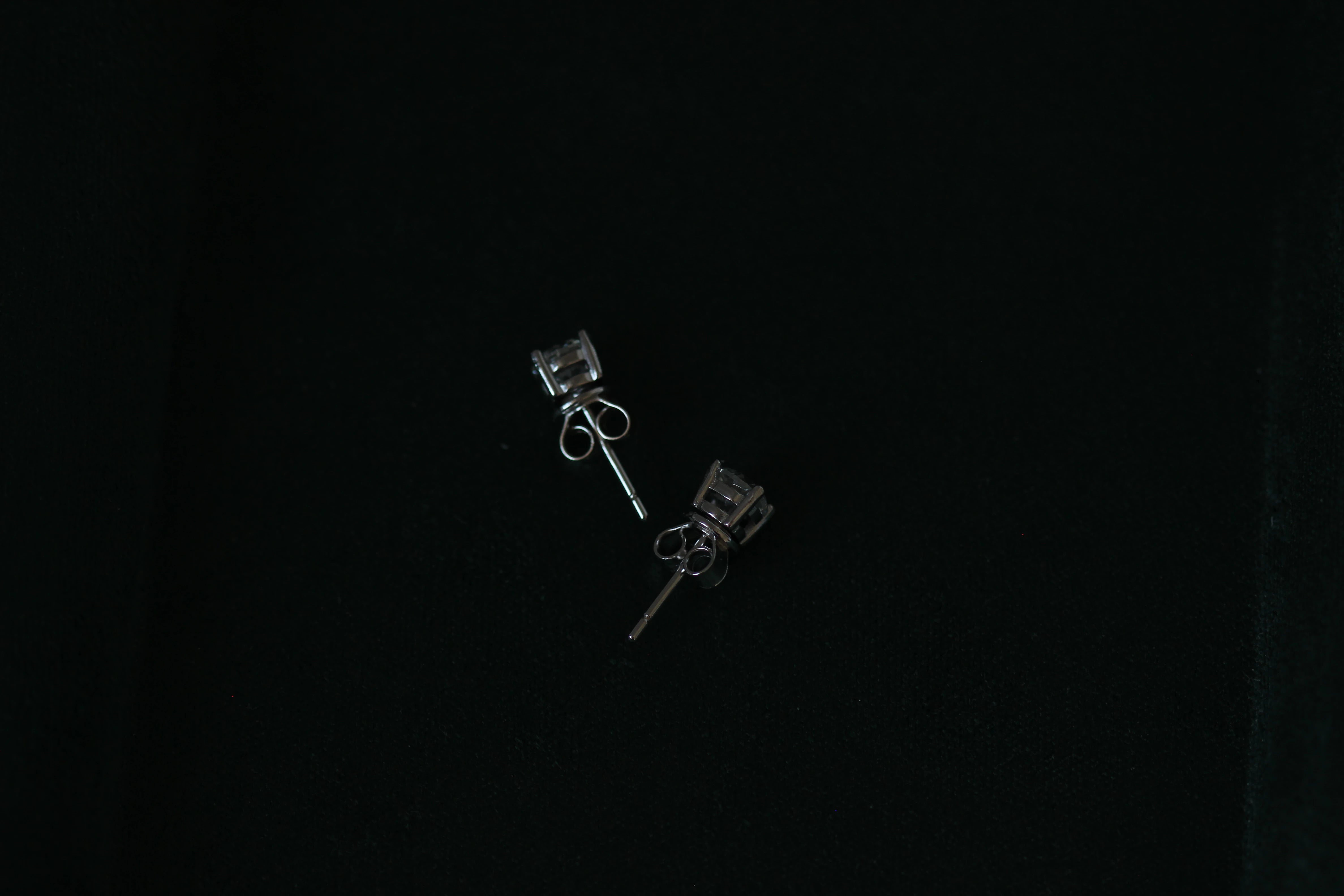Side view of Pair of 1 tcw silver moissanite stud earrings on a black background