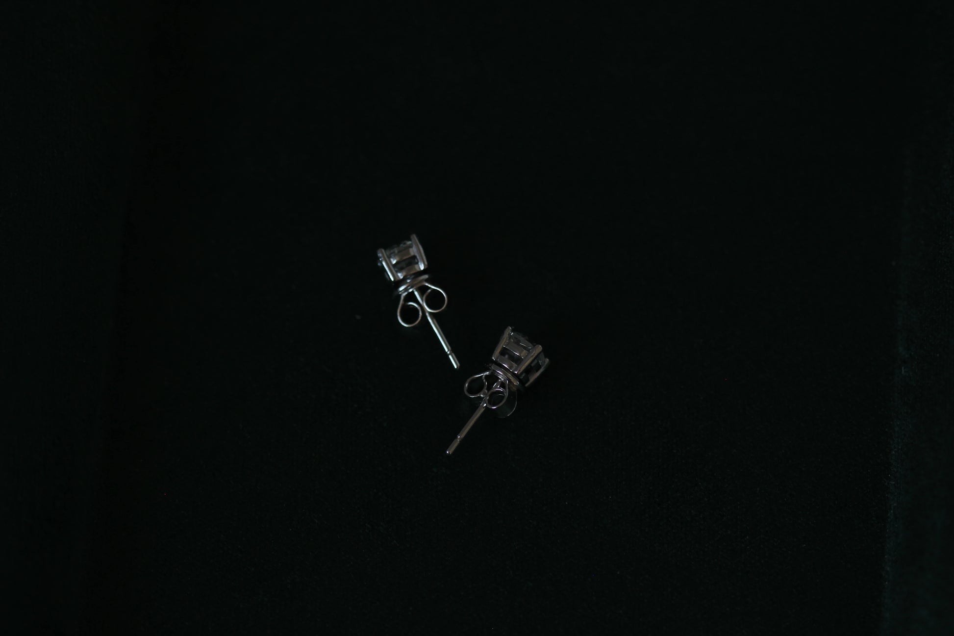 Side view of Pair of 1 tcw silver moissanite stud earrings on a black background