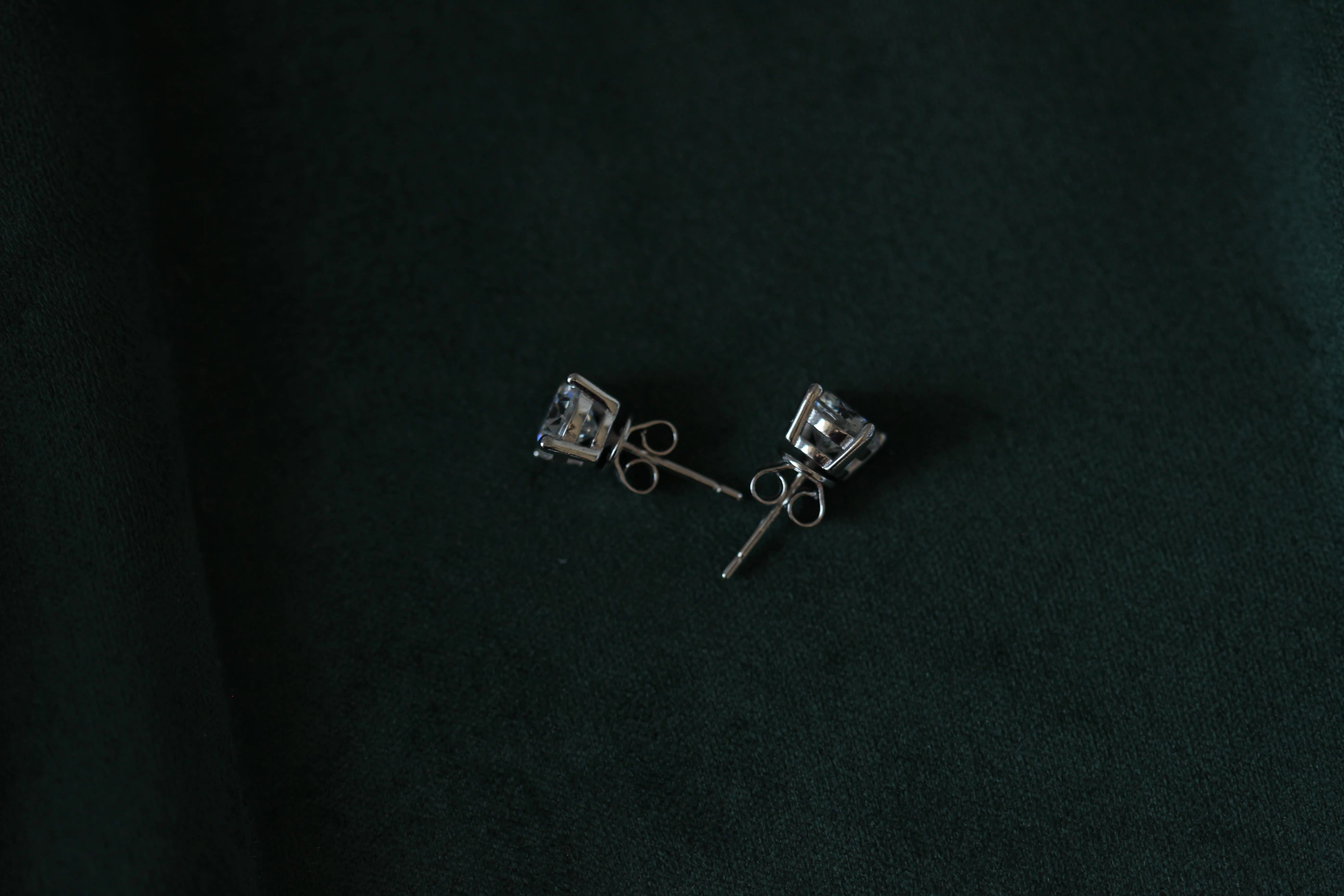 Pair of 2ctw silver moissanite earrings with clear stones on a dark green background