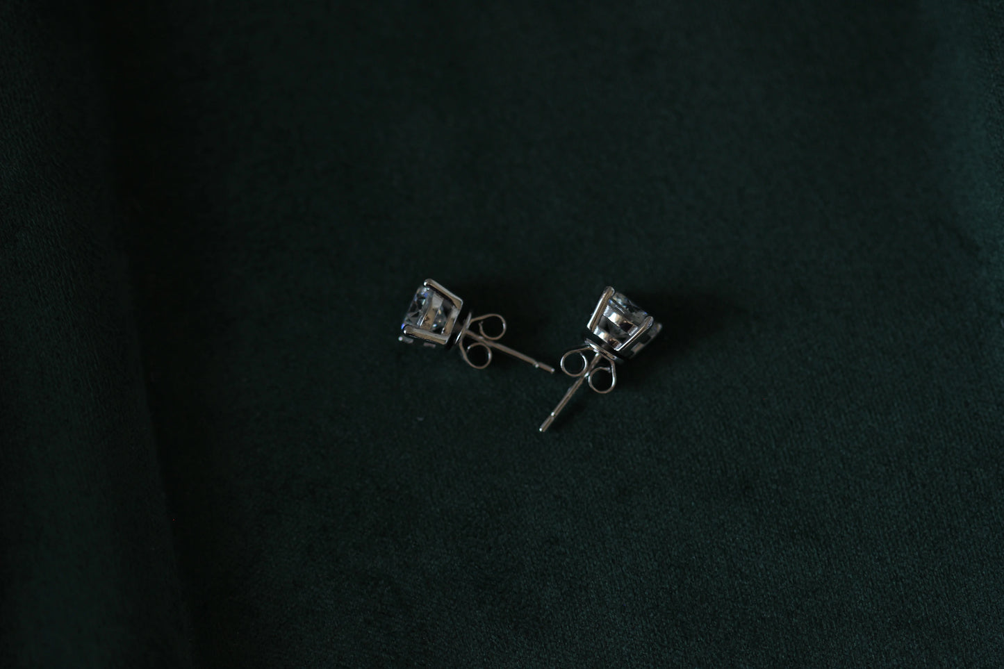 Pair of 2ctw silver moissanite earrings with clear stones on a dark green background