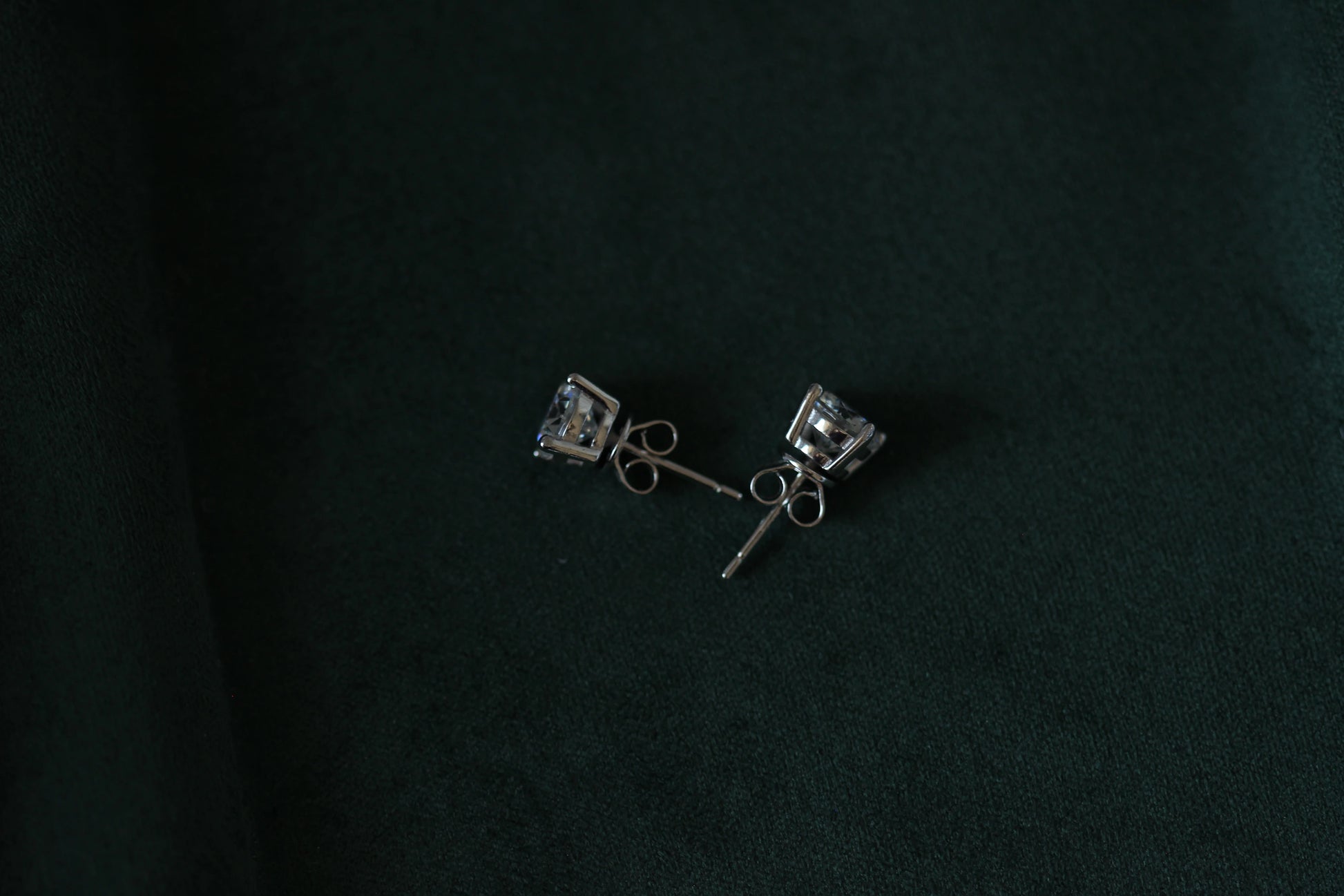 Pair of 2ctw silver moissanite earrings with clear stones on a dark green background