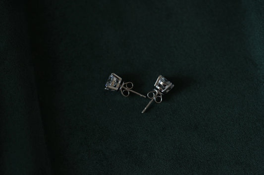 Pair of 2ctw silver moissanite earrings with clear stones on a dark green background
