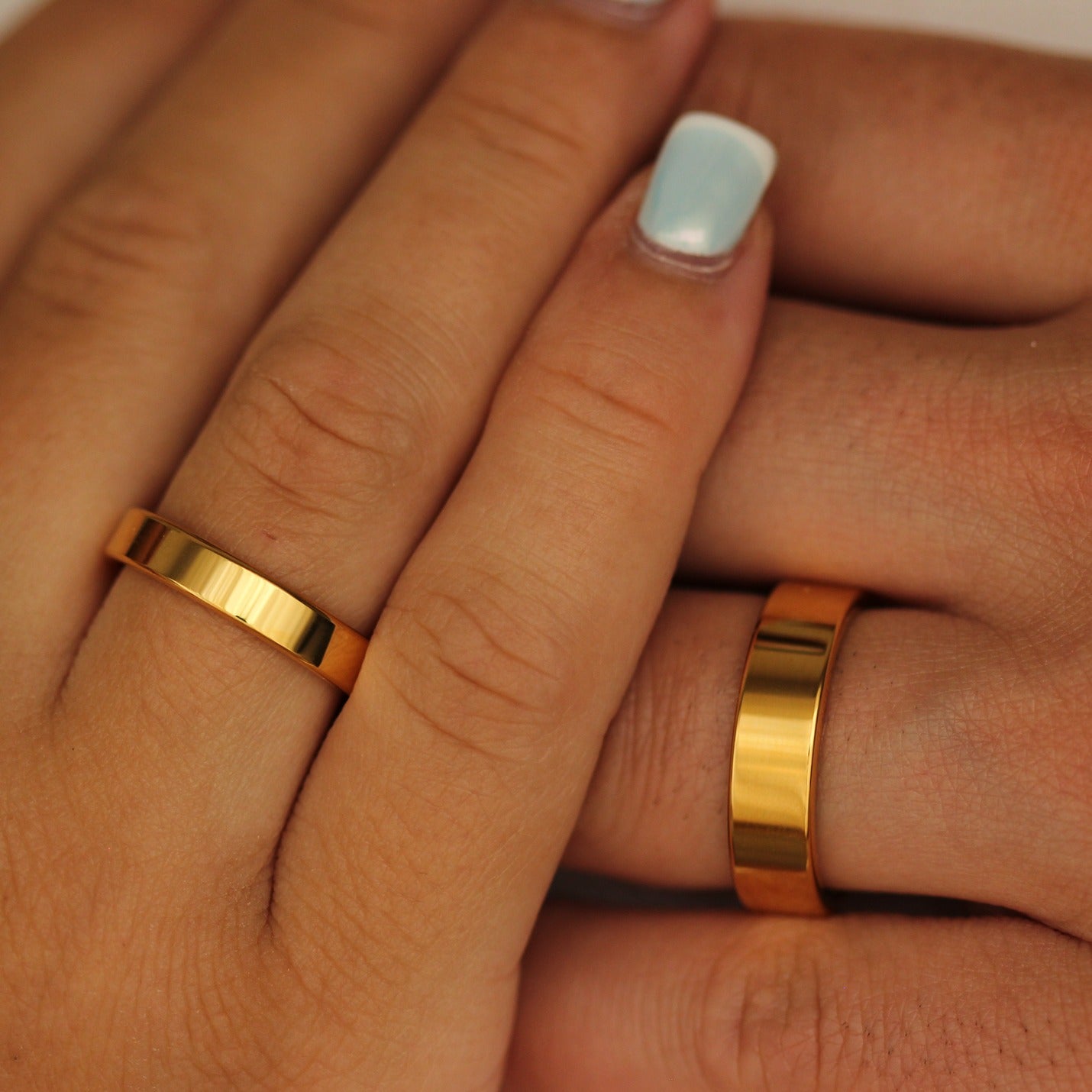 Close-up of two hands wearing two gold flat wedding bands