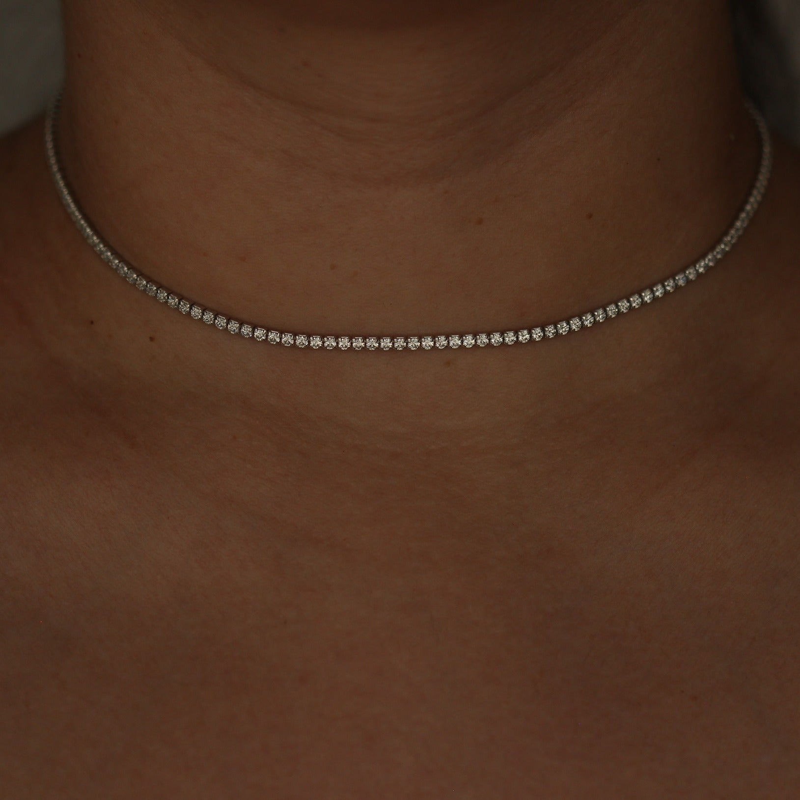 Silver tennis necklace on a person's neck with a blurred background