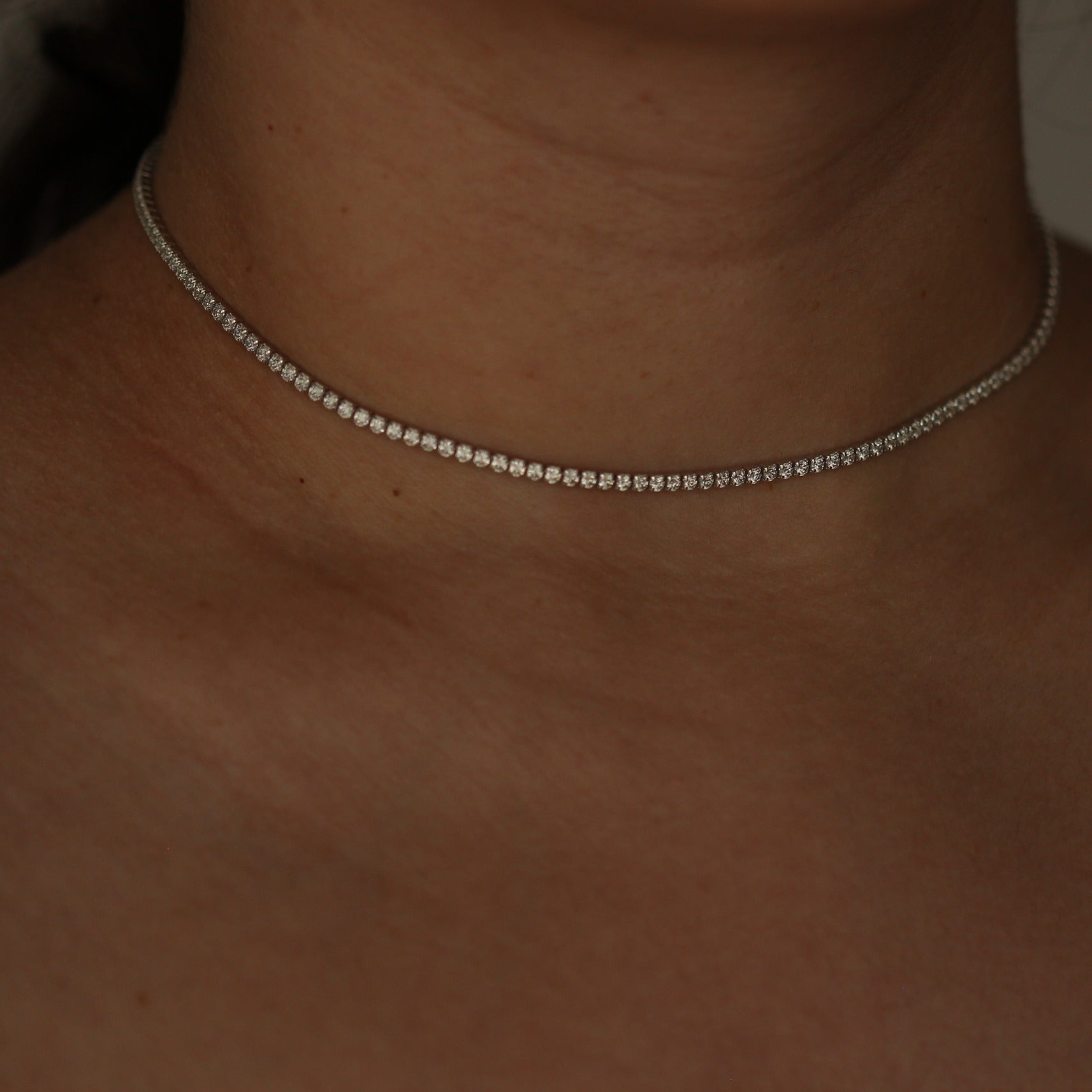 Silver tennis necklace on a person's neck with a blurred background